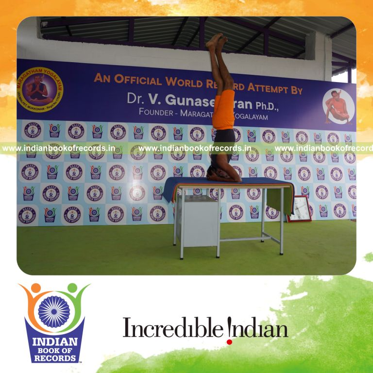 individual holding vama parivrtaikapata sirsasana yoga pose blindfolded on a table for record in Indian Book of Records
