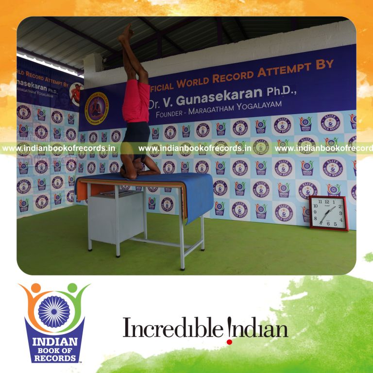 individual holding vama parivrtaikapata sirsasana yoga pose on a table for record in Indian Book of Records