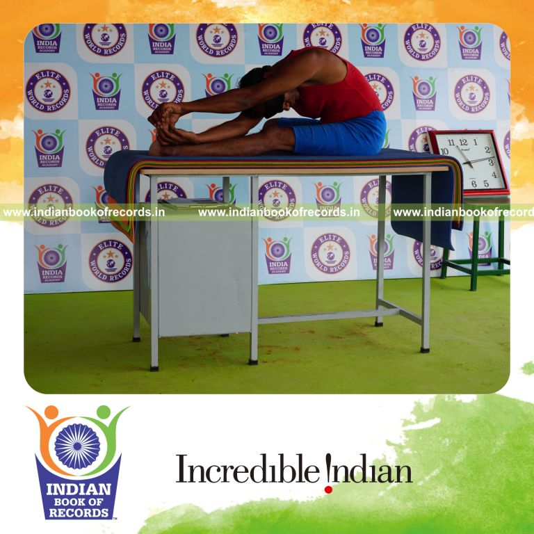 individual holding vama parivrtana janu sirsasana yoga pose blindfolded on a table for record in Indian Book of Records