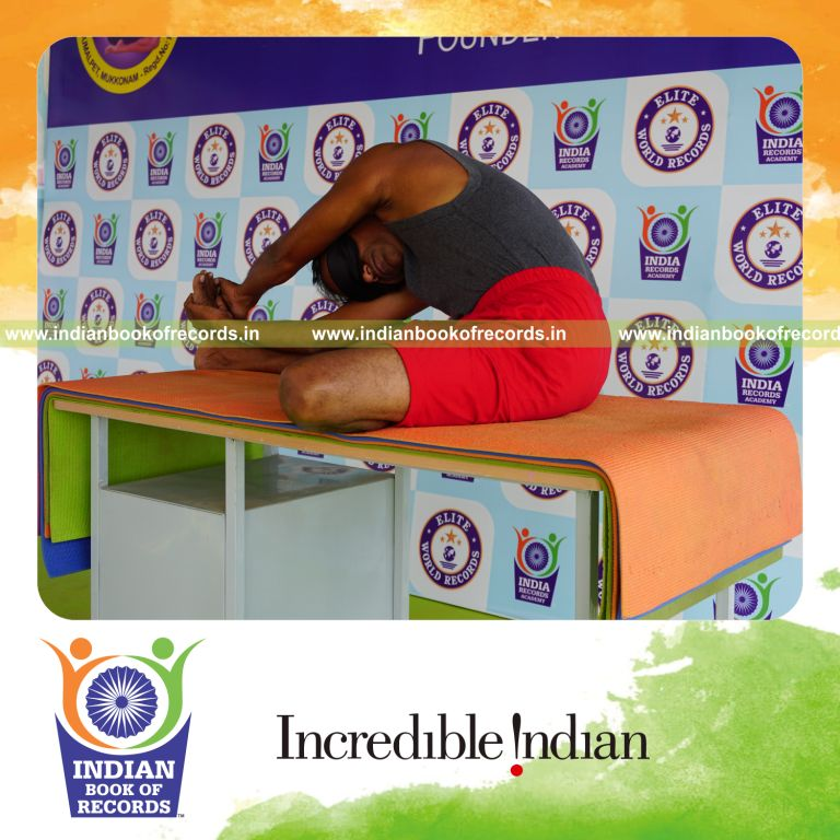 individual holding vama parivrtta janu sirsasana yoga pose blindfolded on a table for record in Indian Book of Records