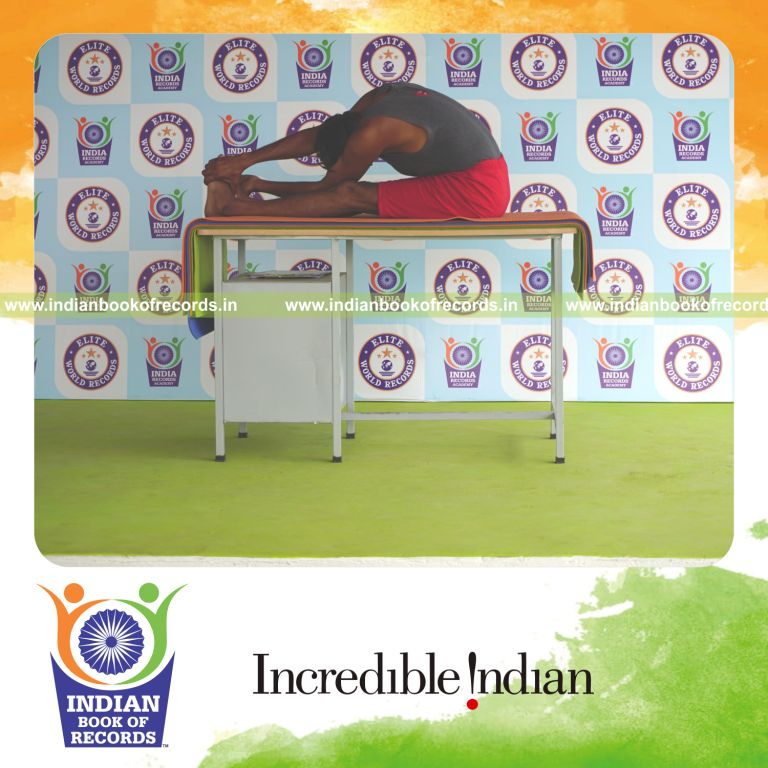 individual holding vama parivrtta paschimottanasana yoga pose blindfolded on a table for record in Indian Book of Records