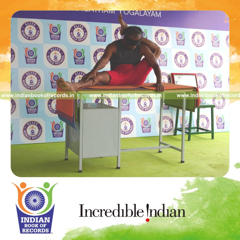 individual holding vama parshwa ekapada sirsasana yoga pose blindfolded on a table for record in Indian Book of Records