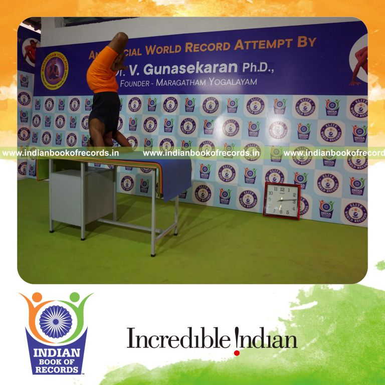 individual holding vama parshwa padma sirsasana yoga pose blindfolded on a table for record in Indian Book of Records