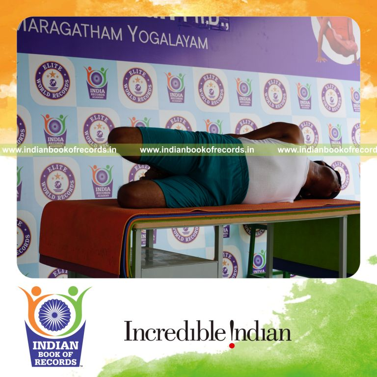 individual holding vama parsva dhanurasana yoga pose blindfolded on a table for record in Indian Book of Records