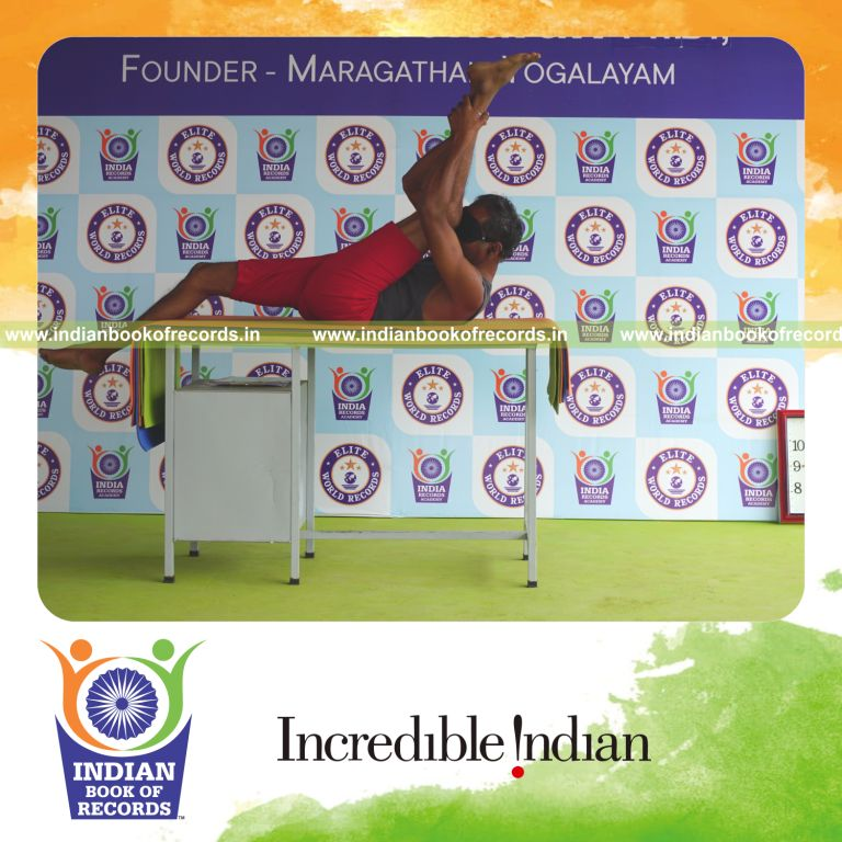 individual holding vama supta padangusthasana yoga pose blindfolded on a table for record in Indian Book of Records