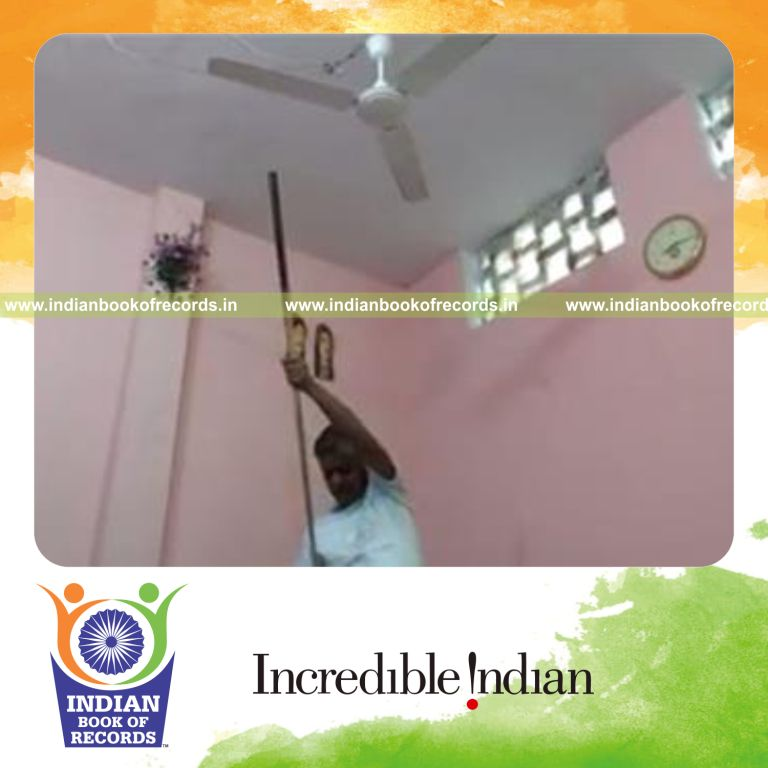 individual balancing phone on pool cue on forehead while sitting for record in Indian Book of Records