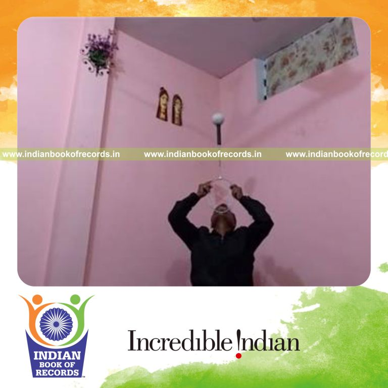 individual balancing softball on badminton racquet handle on chin while kneeling for record in Indian Book of Records