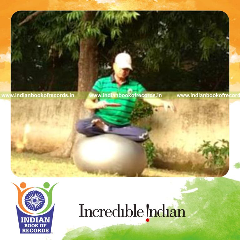 individual bouncing plastic golf ball on paddle while holding lotus pose on exercise ball for record in Indian Book of Records