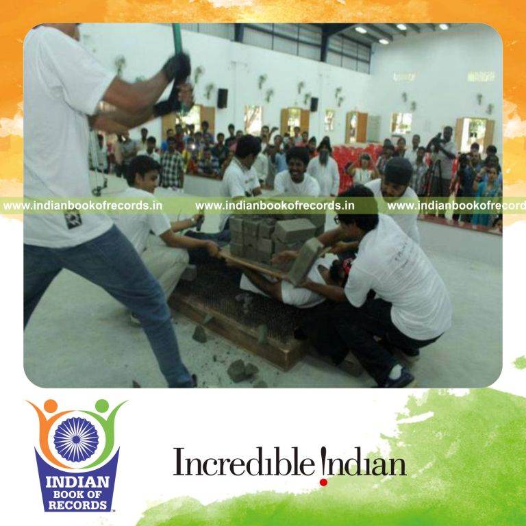 male individual breaking concrete blocks on body while lying on bed of nails for record in Indian Book of Records