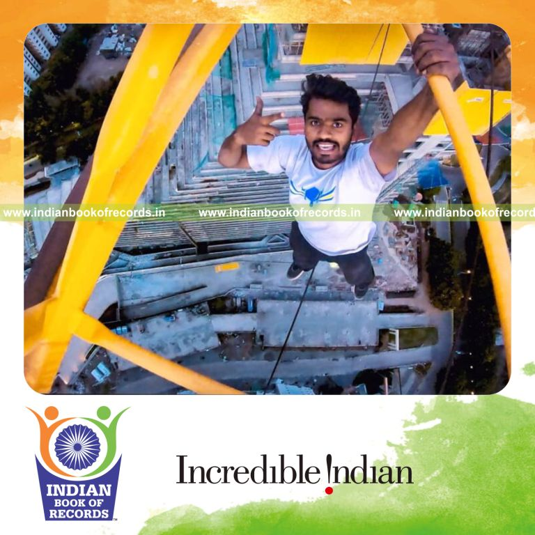 Individual performing a one-handed hang from a crane at a skyscraper height recognized by Indian Book of Records