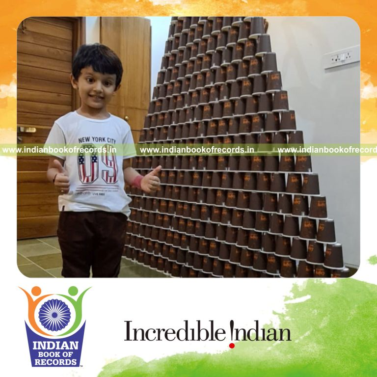 Preschool child building a tall pyramid structure using stacked paper glasses recognized by Indian Book of Records